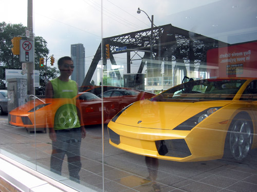 Two lamborghinis in a show room window.  A reflection of Simon in the glass.