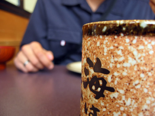 A cup of green tea in the foreground, Rishi in the background.